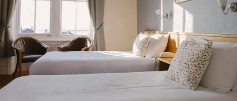 A hotel room with two beds, a chair, a desk, and a window with curtains.
