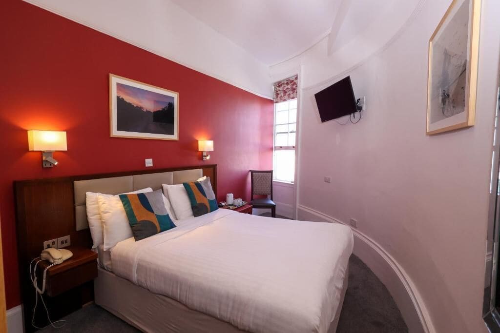 Een hotelkamer met een bed, nachtlampjes, een televisie en een raam.