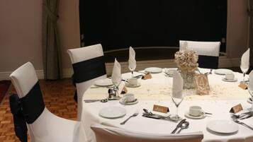 A dining table set for four with white chairs, black sashes, and a vase centerpiece.