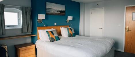 Een slaapkamer met een bed, nachtkastjes, een raam met gordijnen, een deur en een wandlamp.