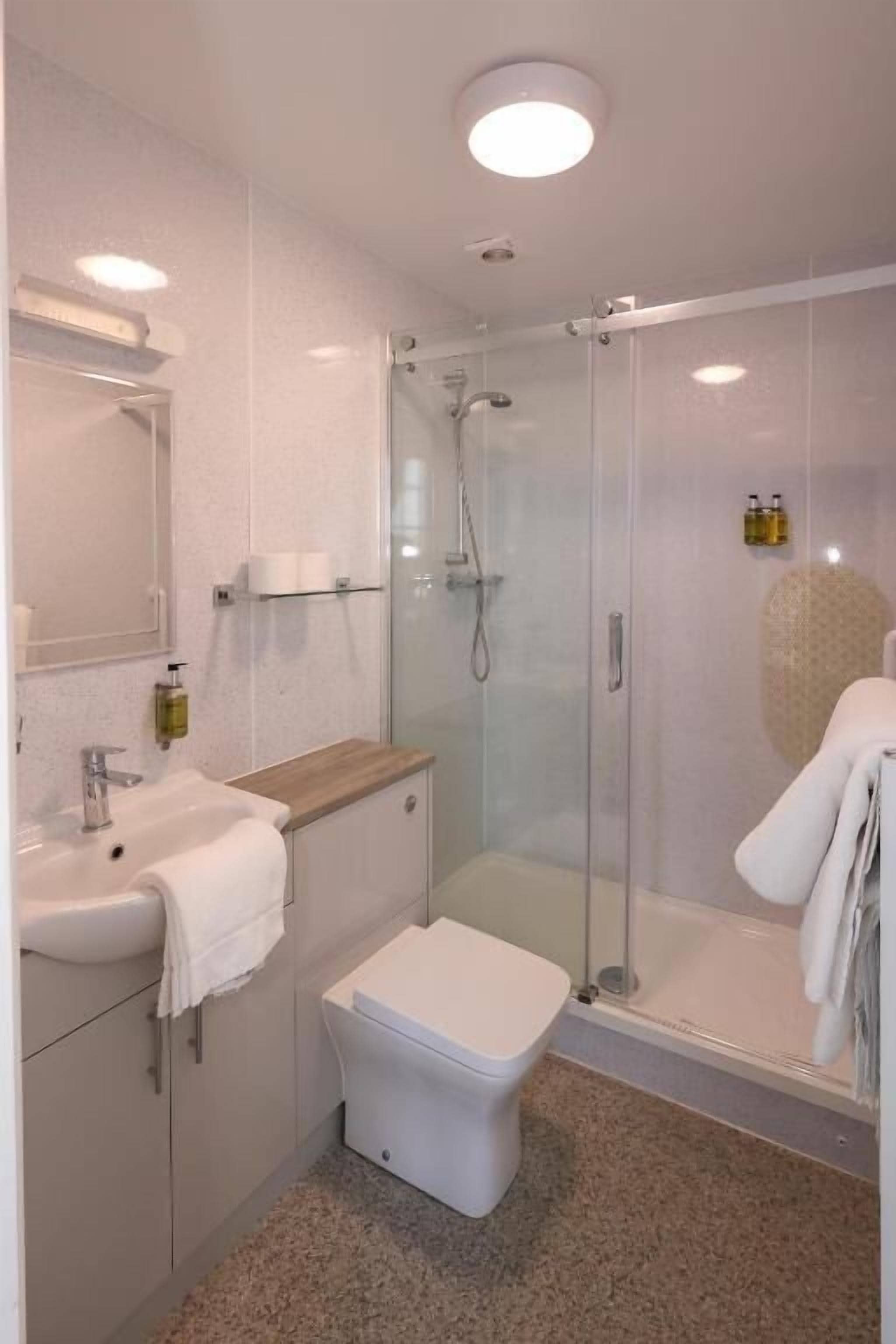 Een moderne badkamer met een douchecabine van glas, een wastafel met handdoek en een toilet.