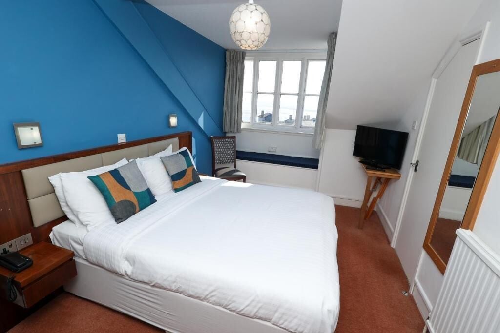 Habitación de hotel con una cama grande, televisión, ventana con cortinas y un espejo.