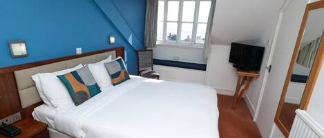 Habitación de hotel con una cama grande, televisión, ventana con cortinas y un espejo.