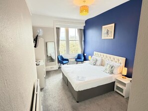 Une chambre à coucher avec un grand lit, des tables de chevet, une chaise, un bureau et une fenêtre avec des rideaux.