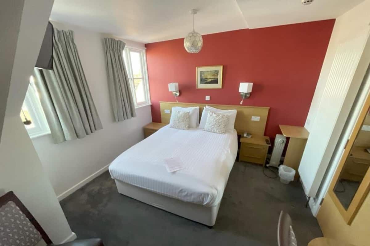 A bedroom with a large bed, bedside tables, a window with curtains, a wall-mounted picture, and a ceiling light fixture.