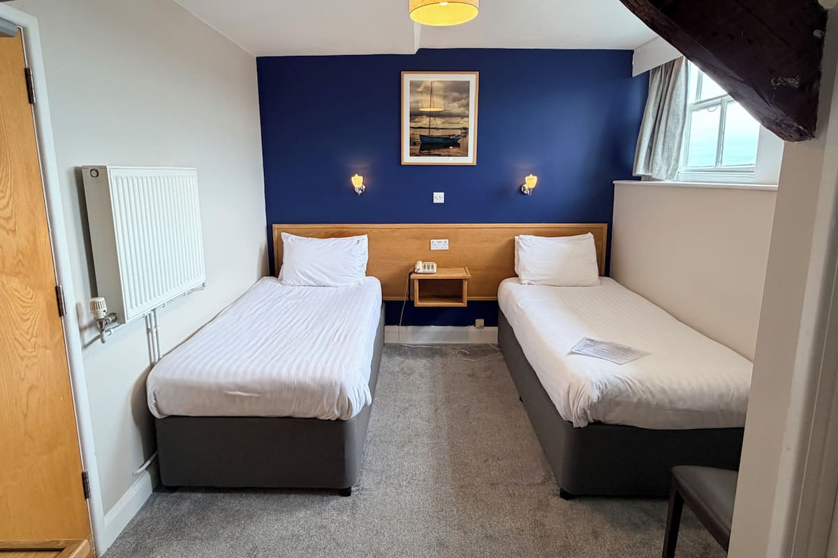 A hotel room with two beds, a wooden headboard, a nightstand, a lamp, a framed picture on the wall, and a window.