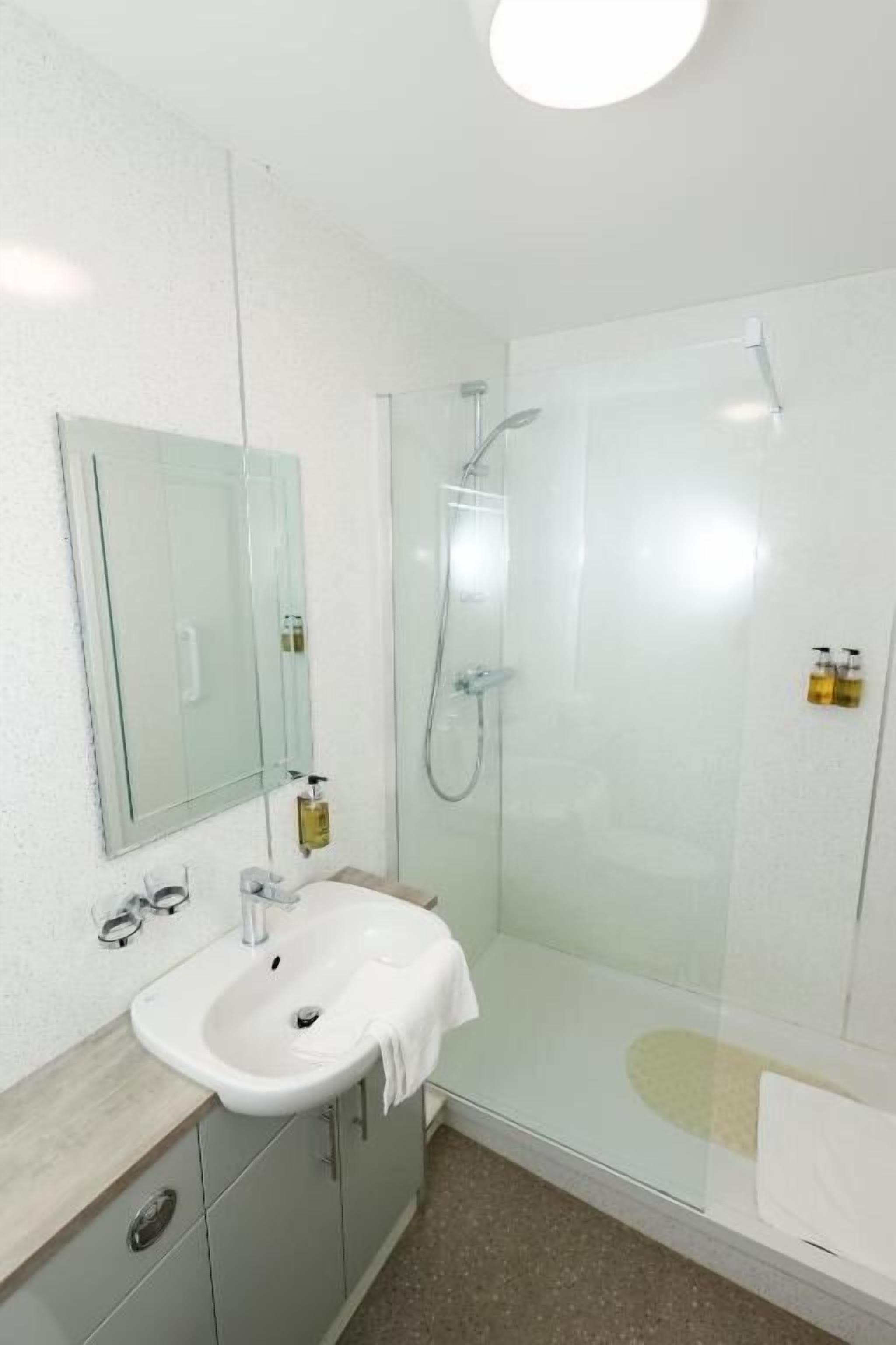 A bathroom with a glass-enclosed shower, a white sink, and a mirror.