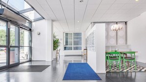 A modern interior with a glass door entrance, a blue carpet, and green chairs. - Ett Smart Kista (Kista)