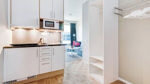 A modern kitchen with white cabinets, a microwave, and a coffee maker. There is a dining area with a blue sofa and a striped rug. - Ett Smart Kista (Kista)