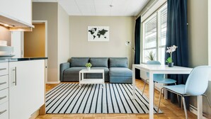 A modern living room with a sofa, a dining table with chairs, a world map on the wall, and a kitchen area with cabinets and a countertop. - Ett Smart Kista (Kista)