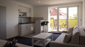 A compact living space with a kitchenette, a sofa, a dining table, and a sliding glass door leading to an outdoor area. - Villa Kiwi (Mikulov)