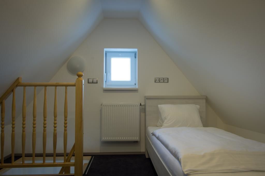 Una habitación pequeña y sencilla con una cama individual, una ventana, un radiador y una escalera de madera.