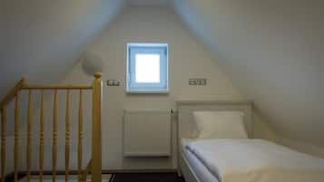 Una habitación pequeña y sencilla con una cama individual, una ventana, un radiador y una escalera de madera.