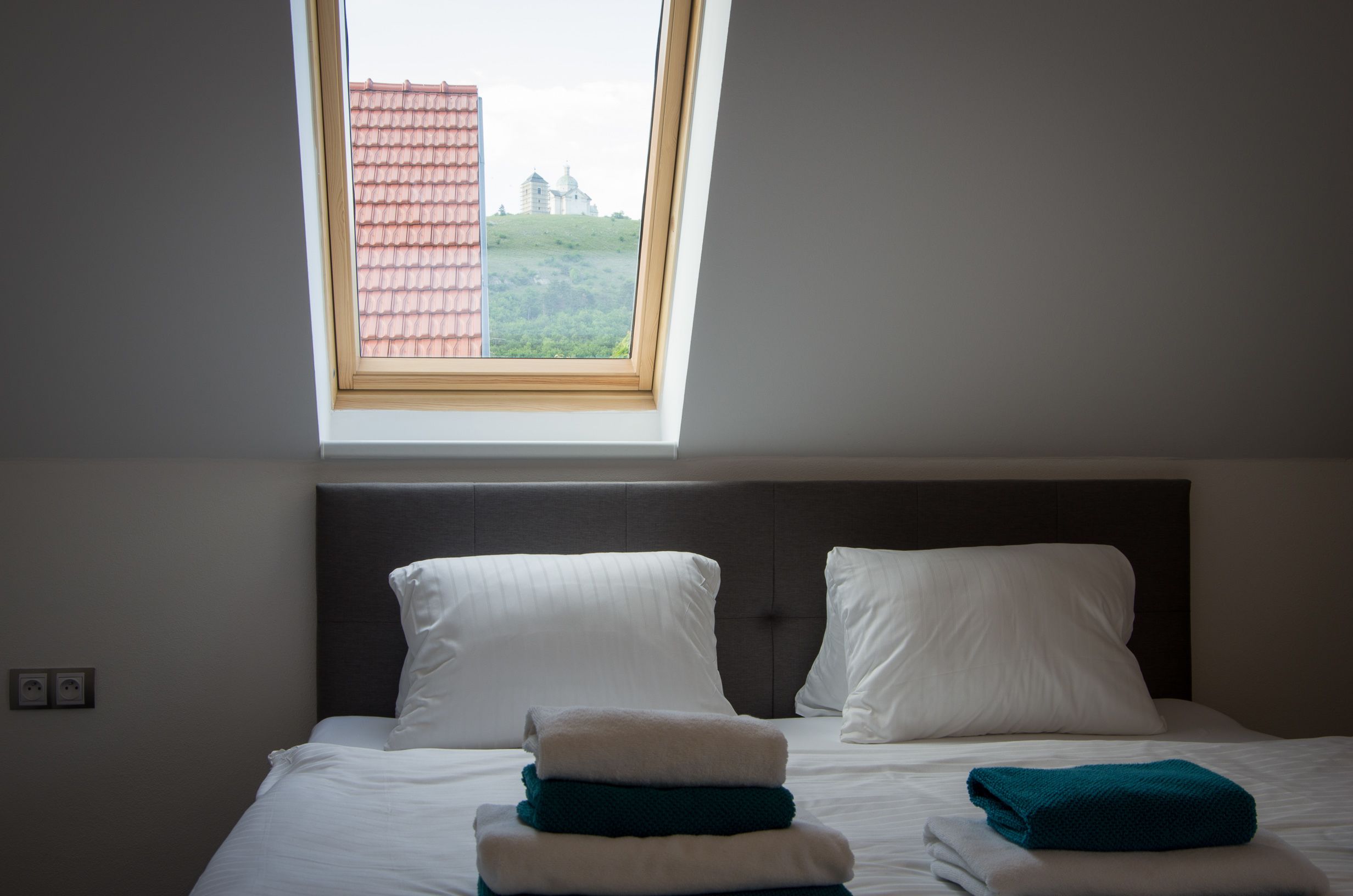 Habitación de hotel con cama, almohadas y vista de un edificio a través de un tragaluz.