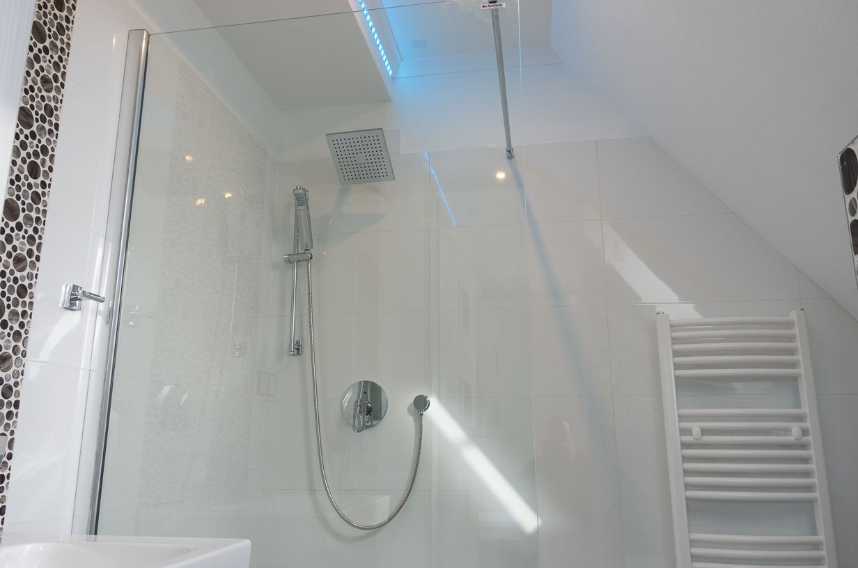 Una ducha moderna con cabina de vidrio, cabezal de ducha de mano y grifería empotrada.