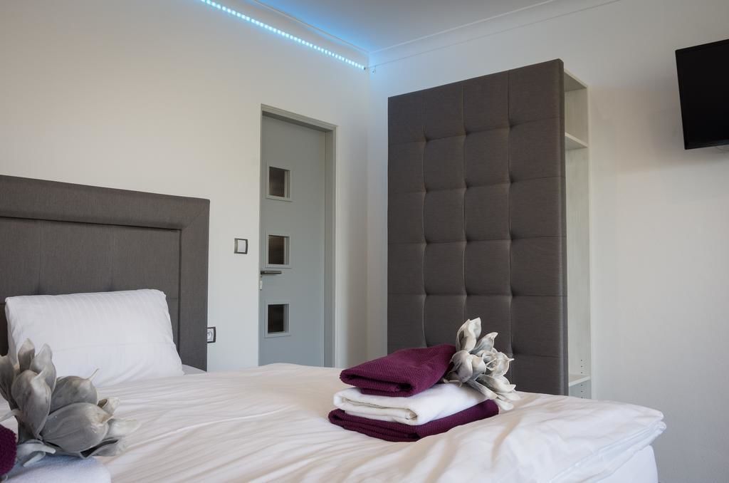Una habitación de hotel con una cama grande, un cabecero gris, un televisor de pantalla plana montado en la pared y una puerta que da a otra habitación.