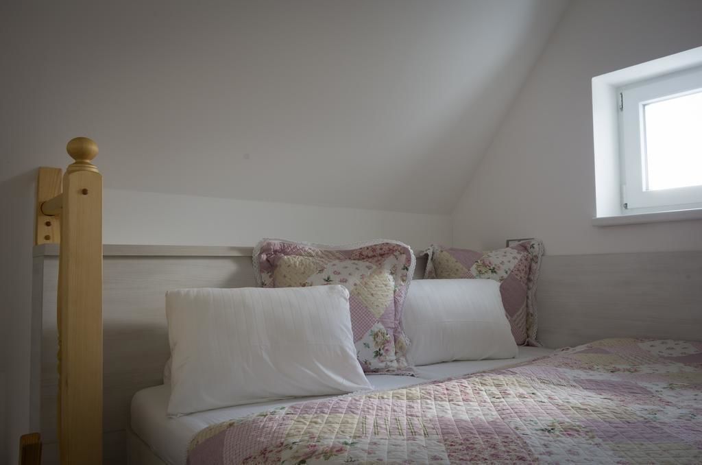 A bedroom with a wooden bed frame, a quilted bedspread, and a window with a view of the sky.