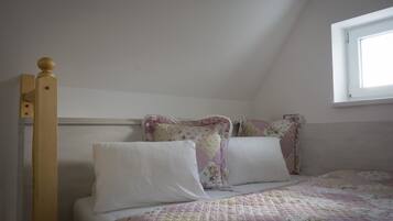 A bedroom with a wooden bed frame, a quilted bedspread, and a window with a view of the sky.