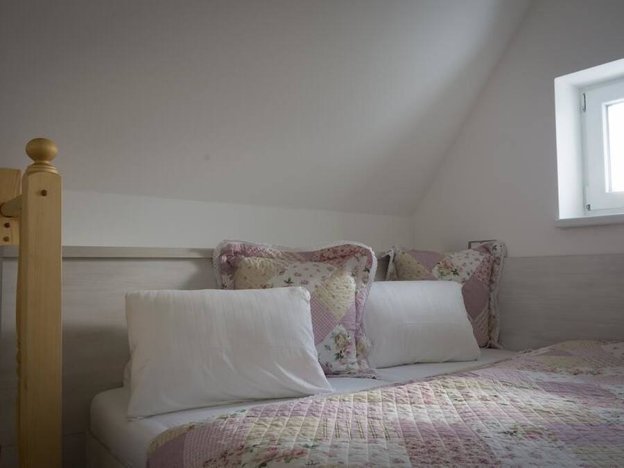 A bedroom with a wooden bed frame, a quilted bedspread, and a window with a view of the sky.