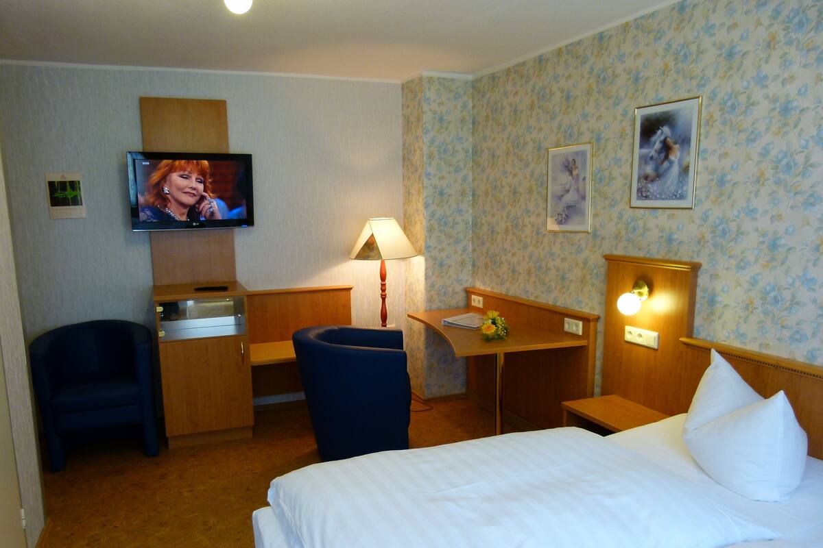 Una habitación de hotel con una cama, un escritorio, una silla, un televisor y una lámpara.