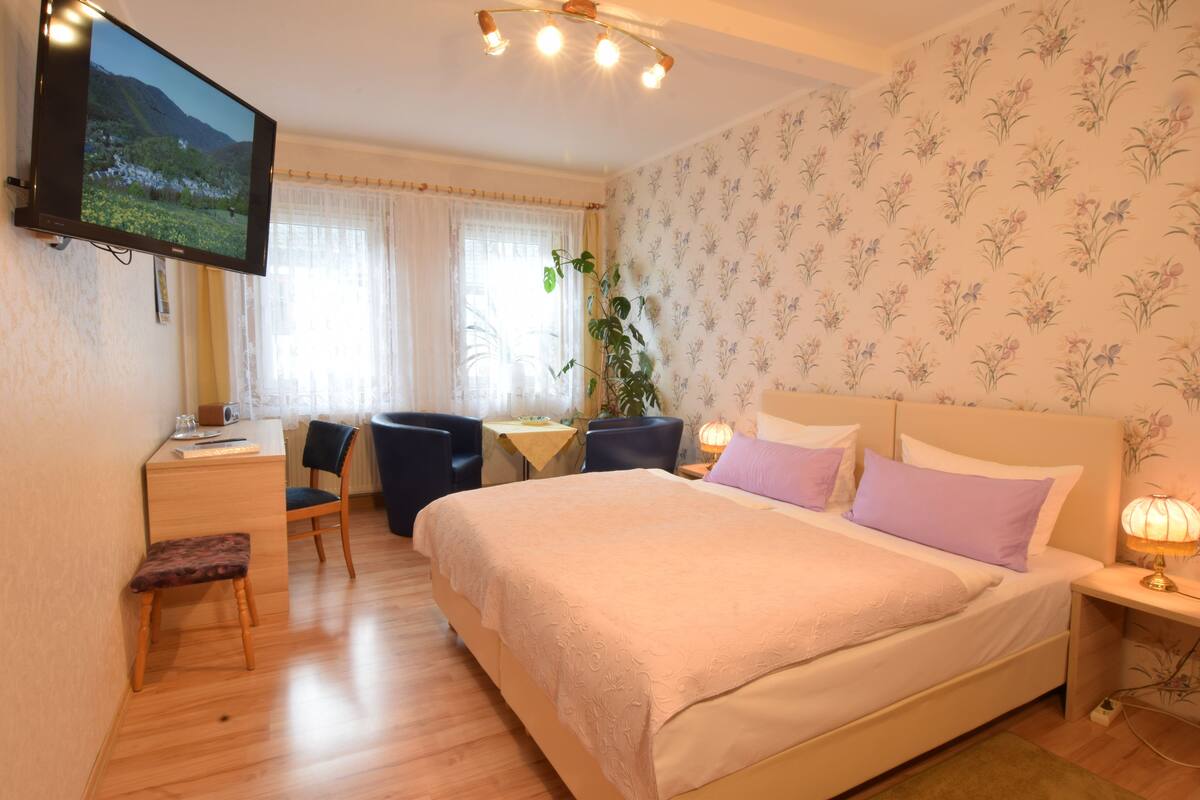 Un dormitorio con una cama, un escritorio, una silla, un televisor y una ventana con cortinas.