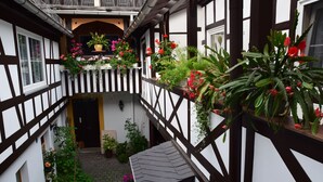 Un edificio tradicional con entramado de madera, un patio central, plantas en macetas y cestas colgantes de flores.