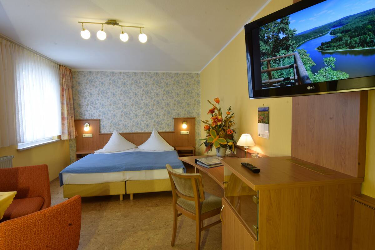 Habitación de hotel con cama, escritorio, silla, televisor y ventana con cortinas.