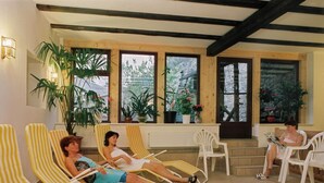 Habitación luminosa con sillones a rayas amarillos y blancos, ventanas amplias y plantas en macetas.