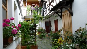 Un patio estrecho con un sendero adoquinado, plantas en macetas y un banco de madera.
