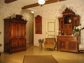 Una habitación con un armario de madera grande, un sillón estampado y una mesita con un jarrón de flores.