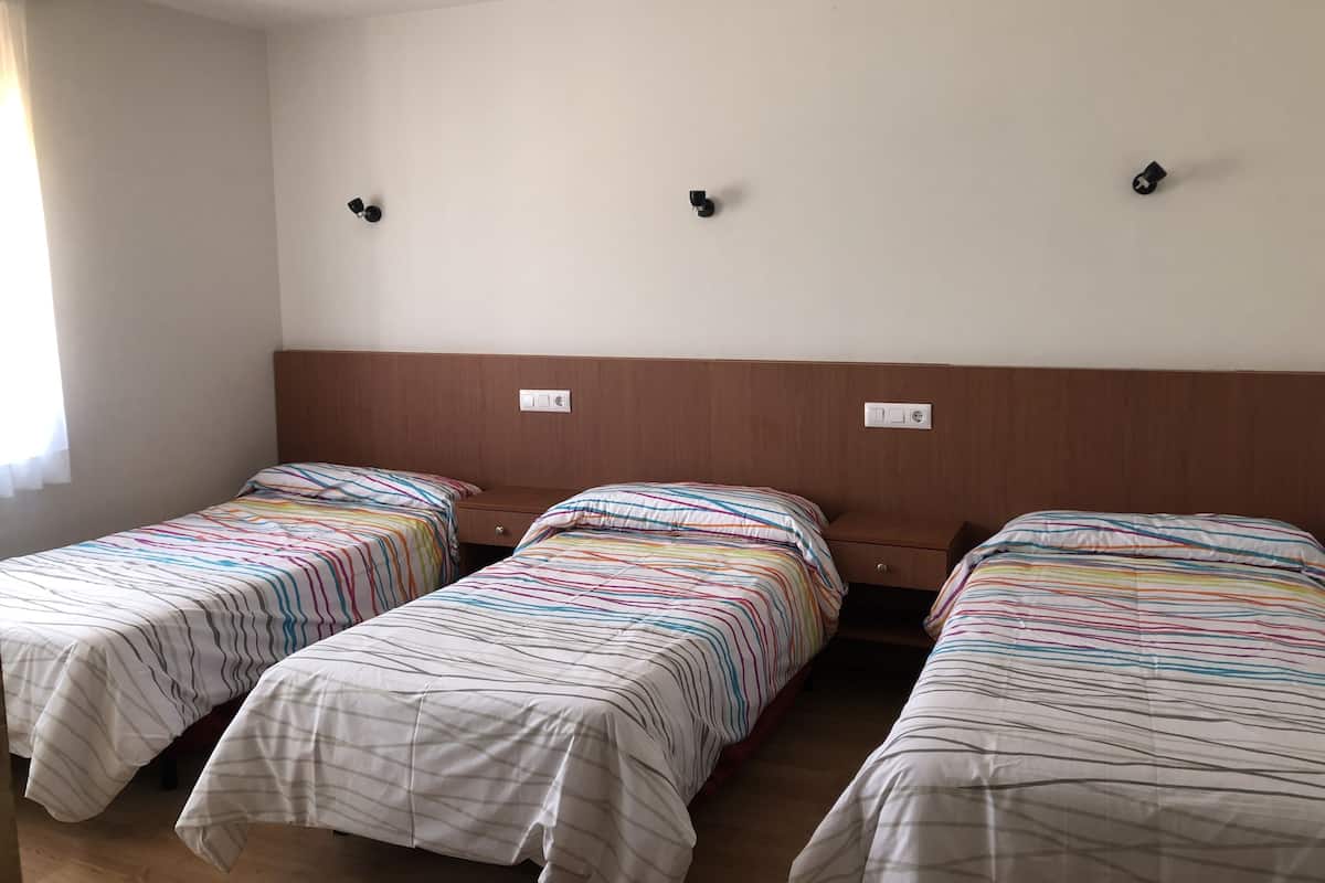 A hotel room with three single beds, each with striped bedding. There are wall-mounted light switches and a wooden headboard.