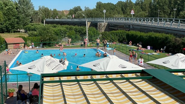 Zona de piscina con un puente al fondo, rodeada de vegetación.