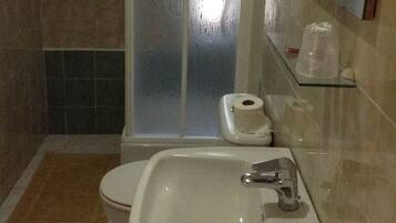 Een badkamer met douche, toilet, wastafel en spiegel.