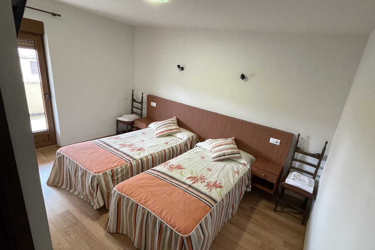 A room with two beds, a wooden headboard, a small table with a chair, and a window.