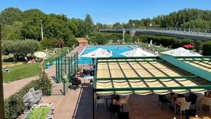 Un área de piscina con varias piscinas, mobiliario exterior y un puente al fondo.