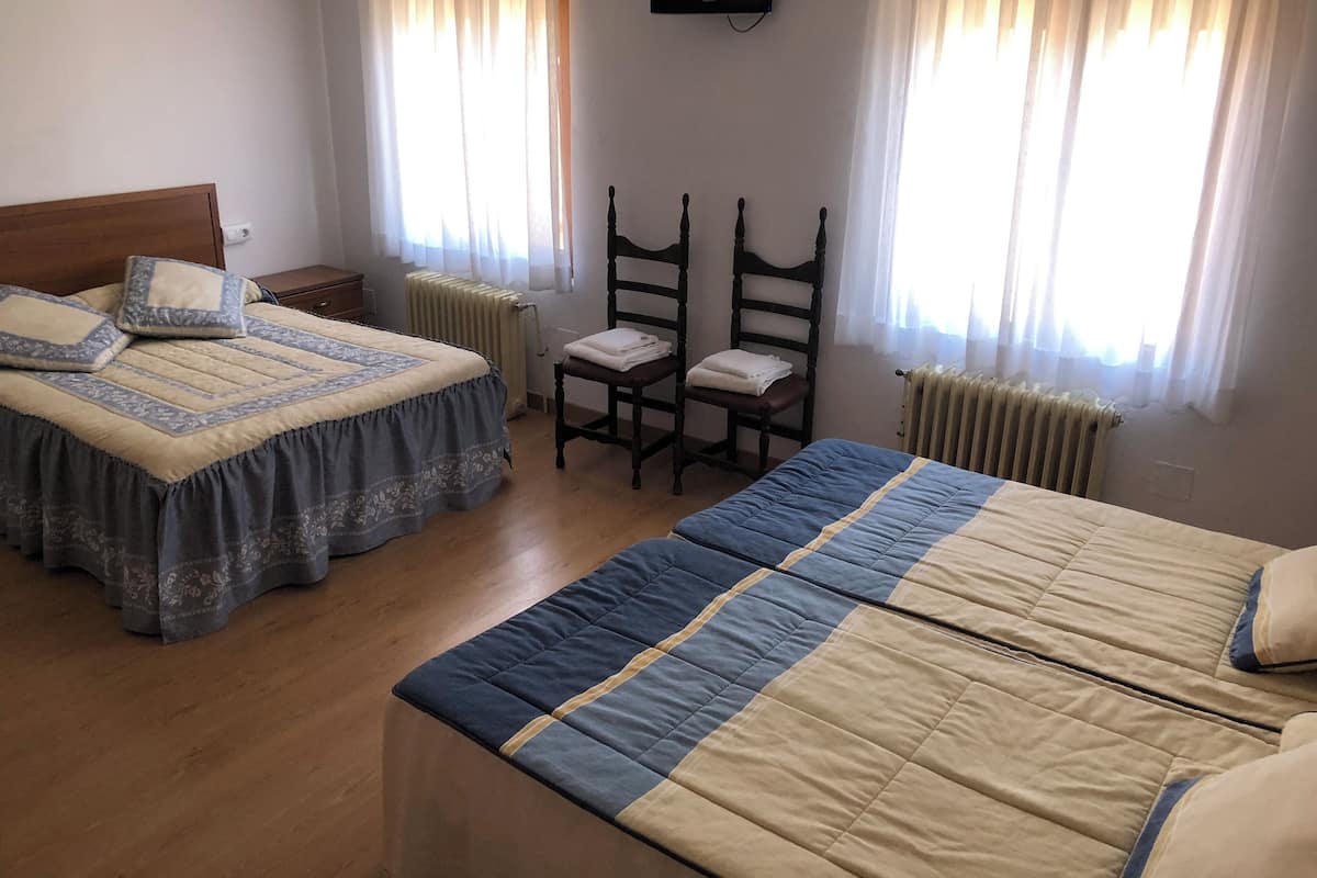 A hotel room with two beds, a chair, a TV, and a window with curtains.
