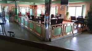 Un restaurante con una barra larga, varias mesas y sillas. Hay un televisor montado en la pared.