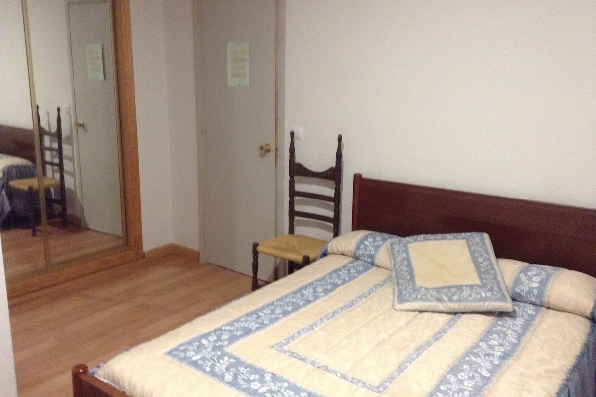 A bedroom with a wooden bed, a chair, a mirror, and a door.