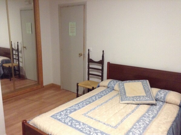 A bedroom with a wooden bed, a chair, a mirror, and a door. - Hostal El Delfin Verde (Villasabariego)