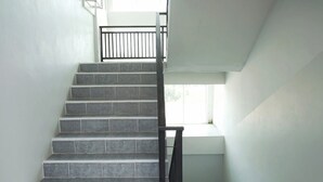 A staircase with grey tiles and a black handrail, leading to a landing with a window. - TF Apartment (Chiang Mai)