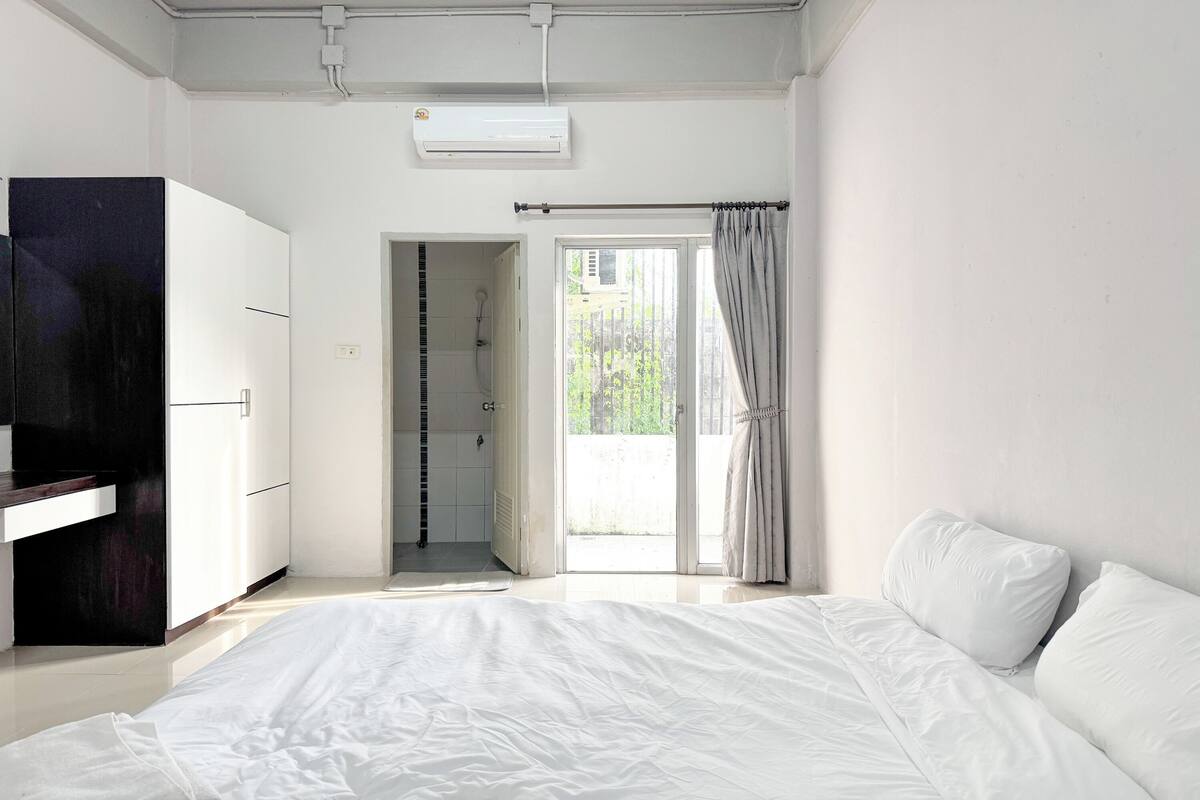 A bedroom with a bed, a wardrobe, a shower, and a view of the outdoors.