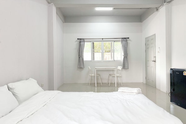A room with a bed, a table with chairs, a window with curtains, and a door.