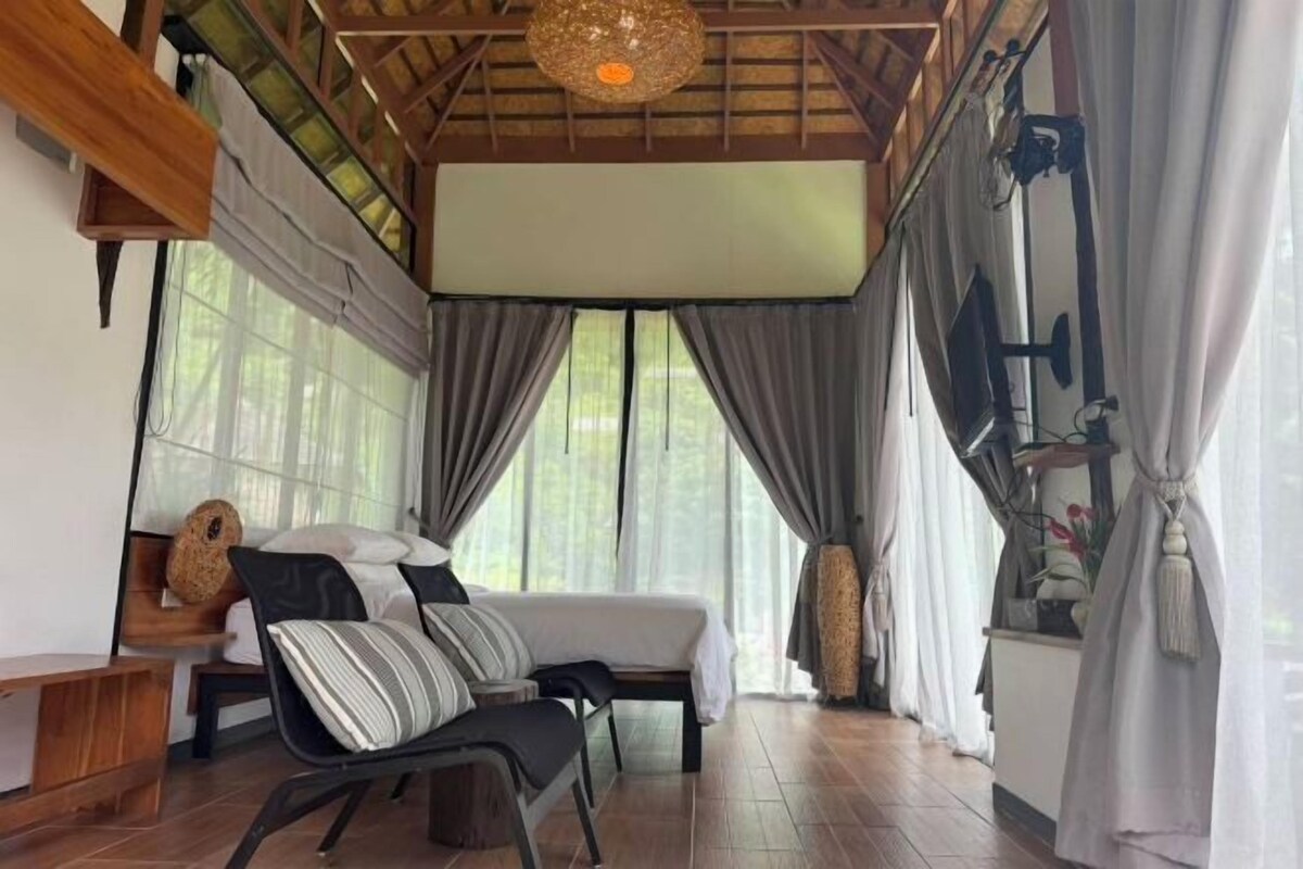 A cozy room with a bed, a chair, and a large window with curtains.
