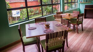 A dining area with a wooden table and chairs, a view of greenery outside, and a sign on the window. - Pilgrims Brook Hotels Ltd (Lagos)