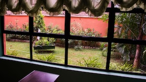 A window with a view of a garden and a red wall. - Pilgrims Brook Hotels Ltd (Lagos)