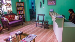 A reception area with a reception desk, a sofa, a bookshelf, and a chair. - Pilgrims Brook Hotels Ltd (Lagos)