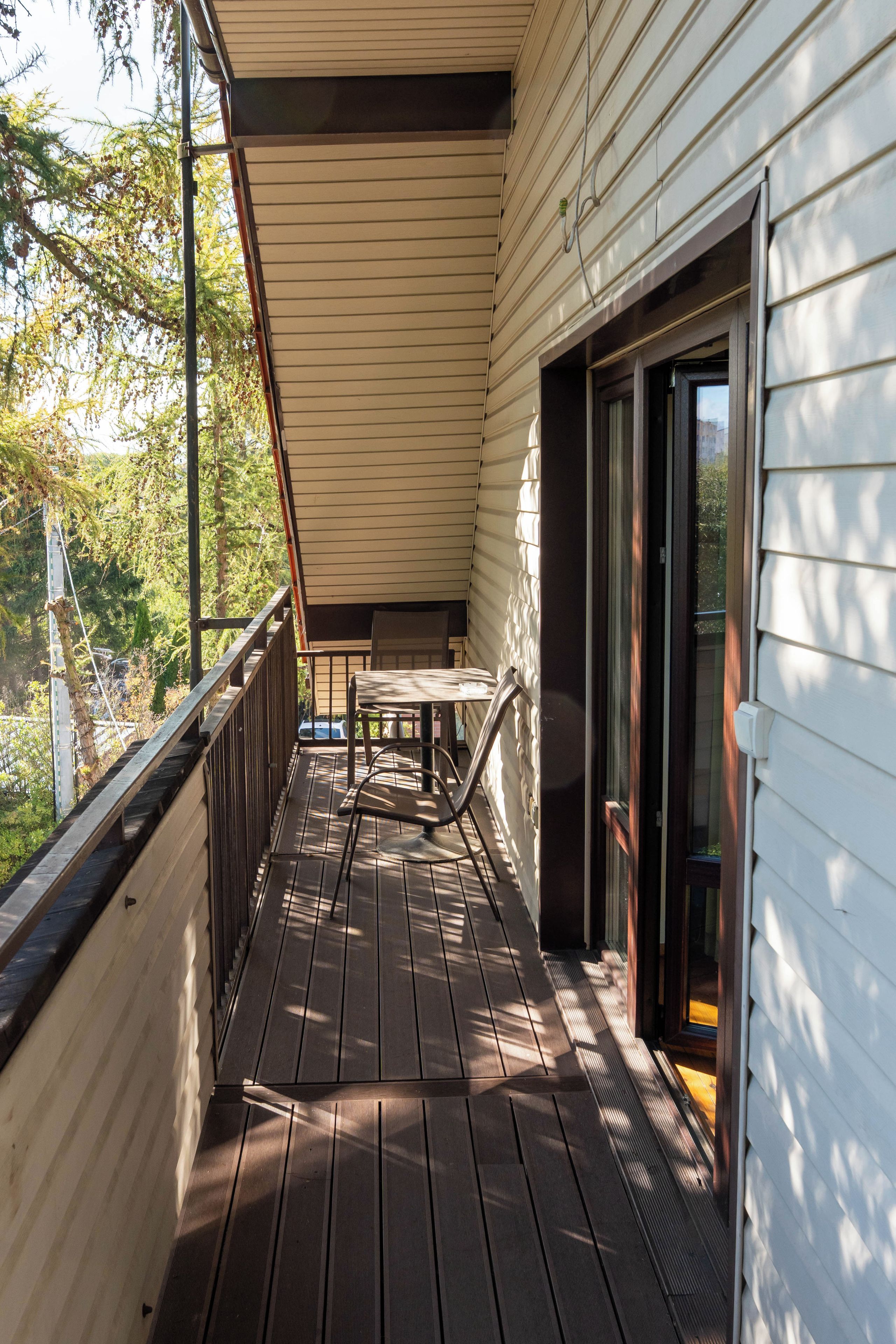A wooden deck with a table and chairs, a sliding glass door, and a view of trees and a car in the background.