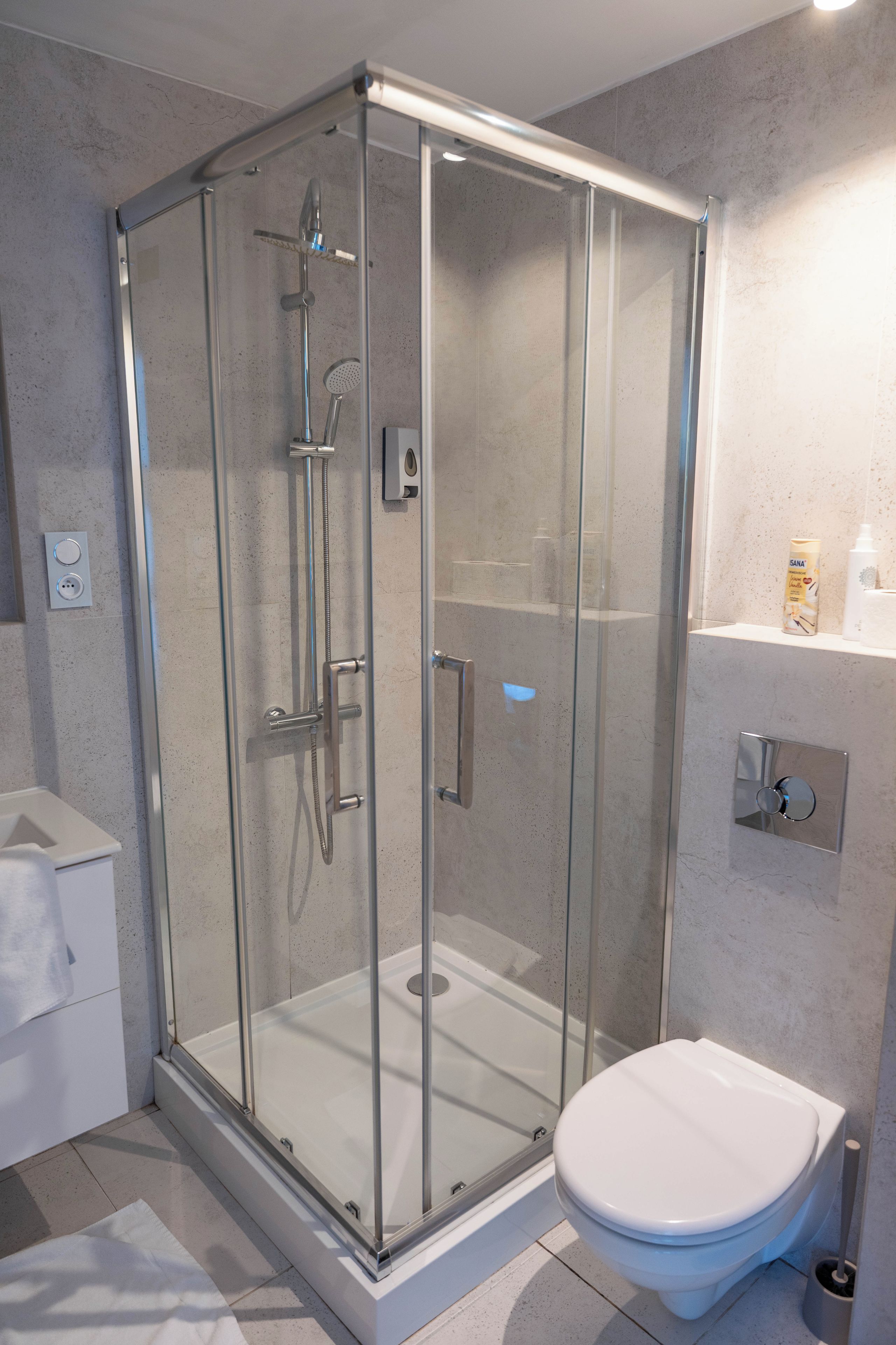 Un baño moderno con ducha de vidrio, inodoro blanco y un pequeño estante con artículos de tocador.