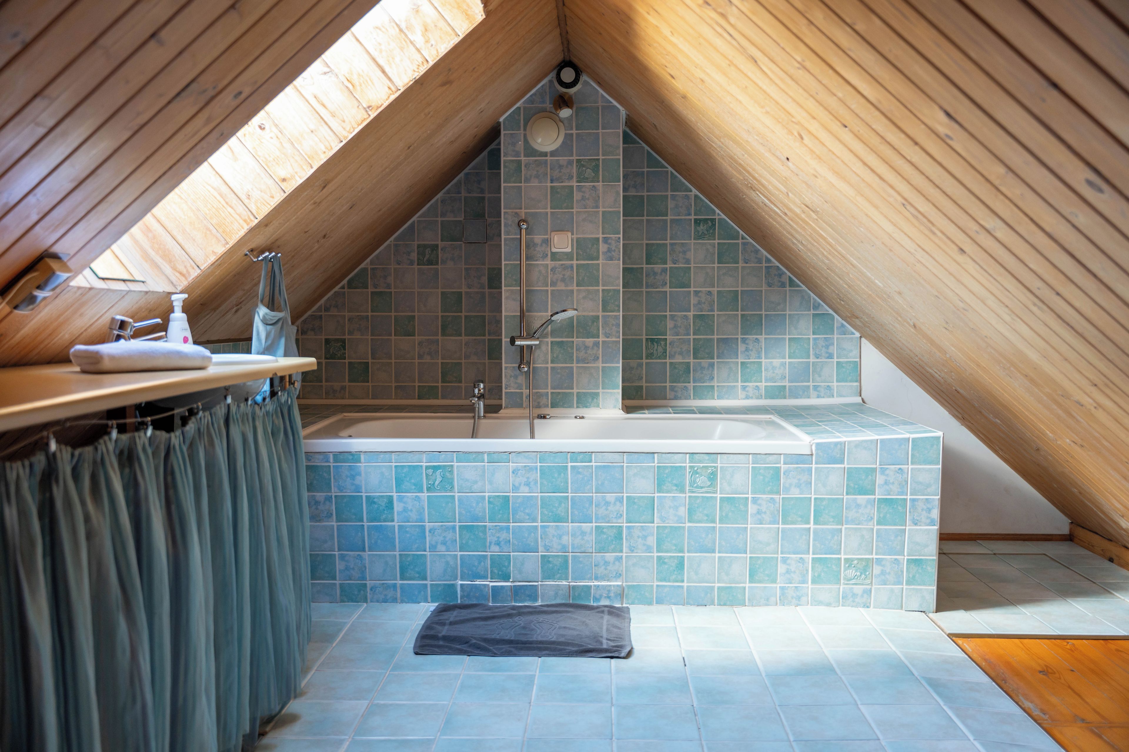 Ein Badezimmer mit schrägverdeckelter Decke, einer Badewanne und einer Duschkabine.