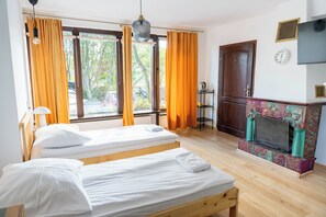 A room with two beds, a fireplace, a clock, and a window with curtains. - Villa Zosieńka (Gdansk)